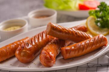 Würstel cotti su piatto bianco con limone e salse. Specialità di carne.