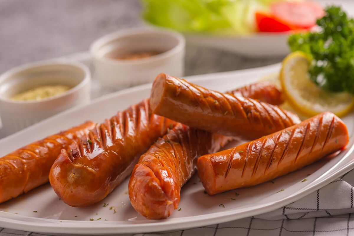 Würstel cotti su piatto bianco con limone e salse. Specialità di carne.