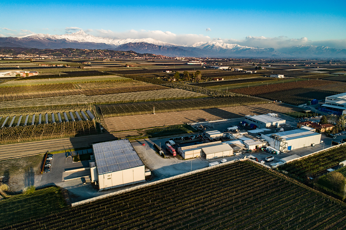 Stabilimento Carni Dock Lagnasco. Veduta aerea, campi coltivati e montagne innevate sullo sfondo.