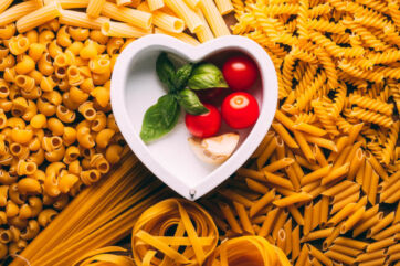 Pasta italiana assortita con pomodori, basilico e aglio in ciotola a forma di cuore. Ricetta tradizionale.