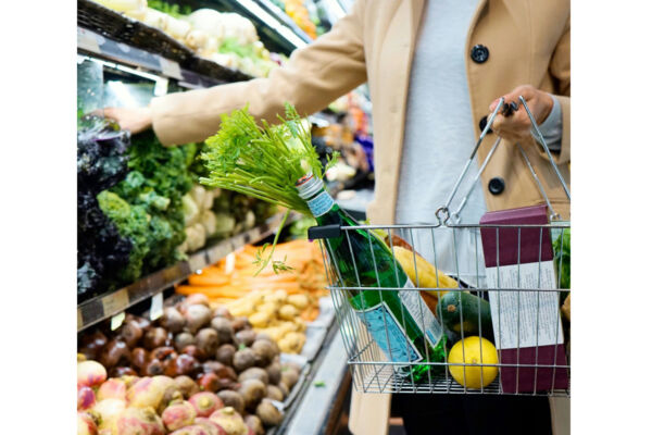 Donna al supermercato con carrello pieno di verdure fresche e acqua. Spesa alimentare.