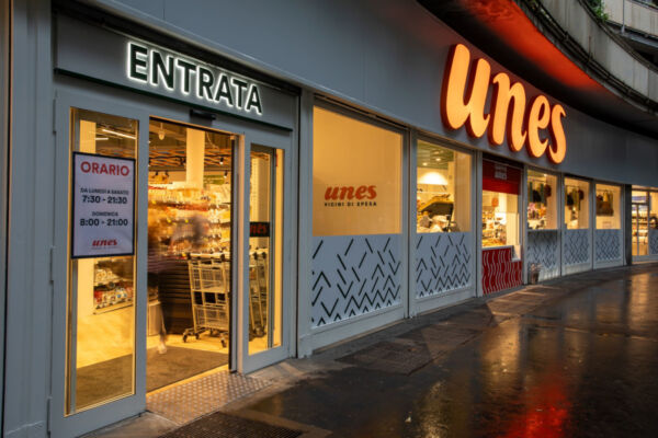 Esterno supermercato Unes. Insegna Entrata e logo Unes illuminato. Orari negozio visibili. Spesa facile.