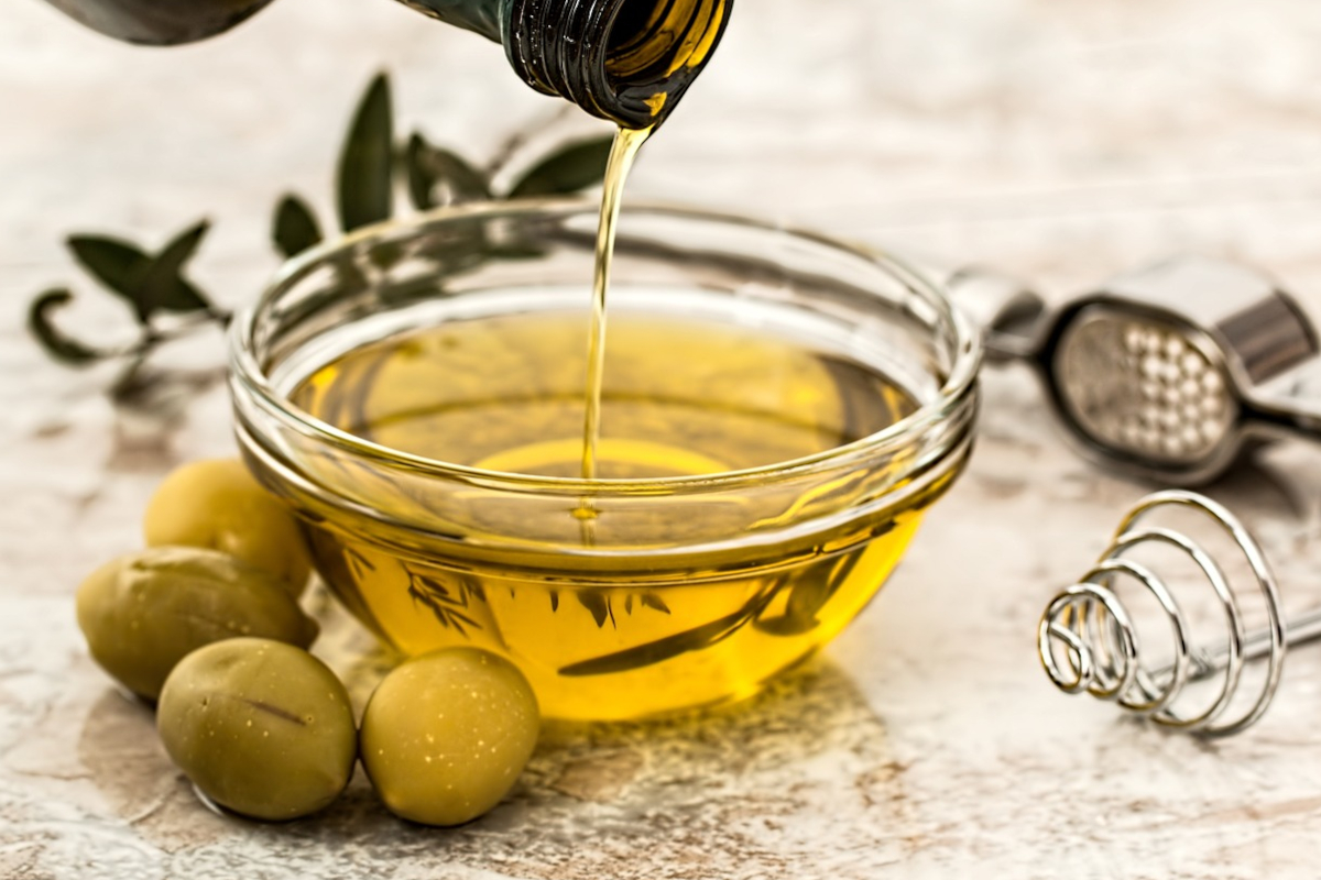 Olio extravergine d'oliva versato in ciotola con olive verdi. Condimento sano e gustoso.