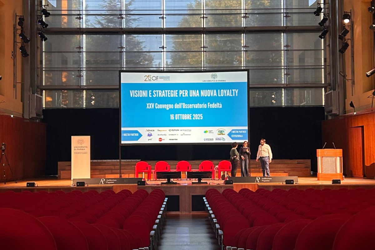 Osservatorio Fedeltà 2025: Convegno loyalty, strategie e visioni future. Sala conferenze con palco e sedie rosse.