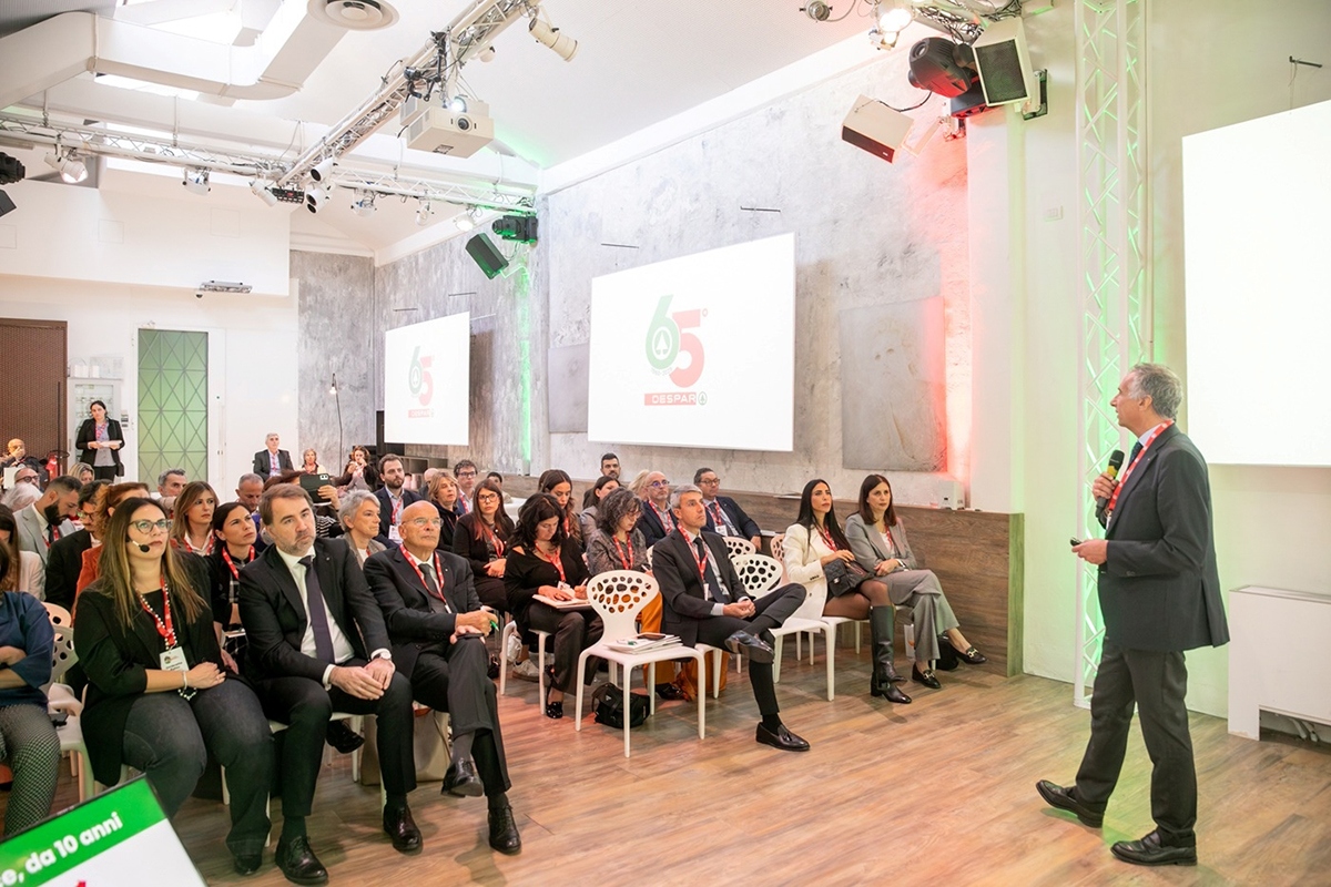 Evento Despar Italia: relatore e pubblico celebrano i 65 anni del marchio. Insegna Despar proiettata sullo schermo.