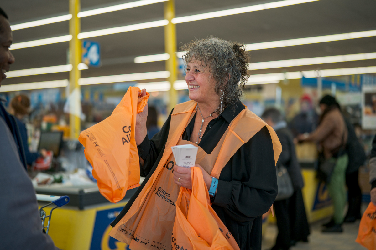 Volontaria sorridente alla Colletta Alimentare con sacchetti arancioni. Raccolta alimentare, Banco Alimentare.