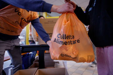 Volontari alla Colletta Alimentare: sacchetto arancione pieno di cibo donato al Banco Alimentare.