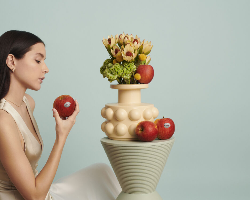 Nuova collezione Envy™. Donna con mela Envy, vaso di fiori. Eleganza e gusto in ogni morso.