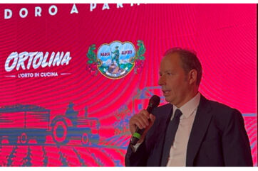 Rodolfi Aldo parla della campagna pomodoro 2025. Logo Ortolina, Marca Alpino e trattore sullo sfondo.