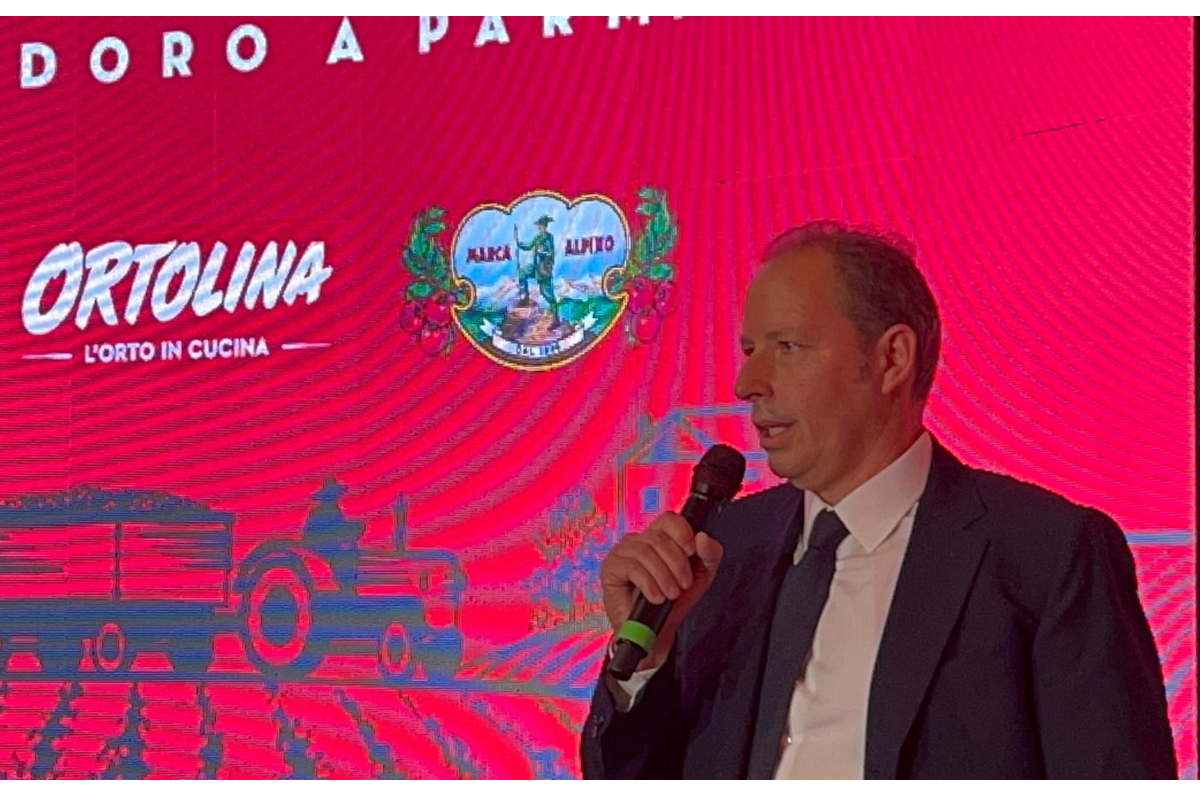 Rodolfi Aldo parla della campagna pomodoro 2025. Logo Ortolina, Marca Alpino e trattore sullo sfondo.
