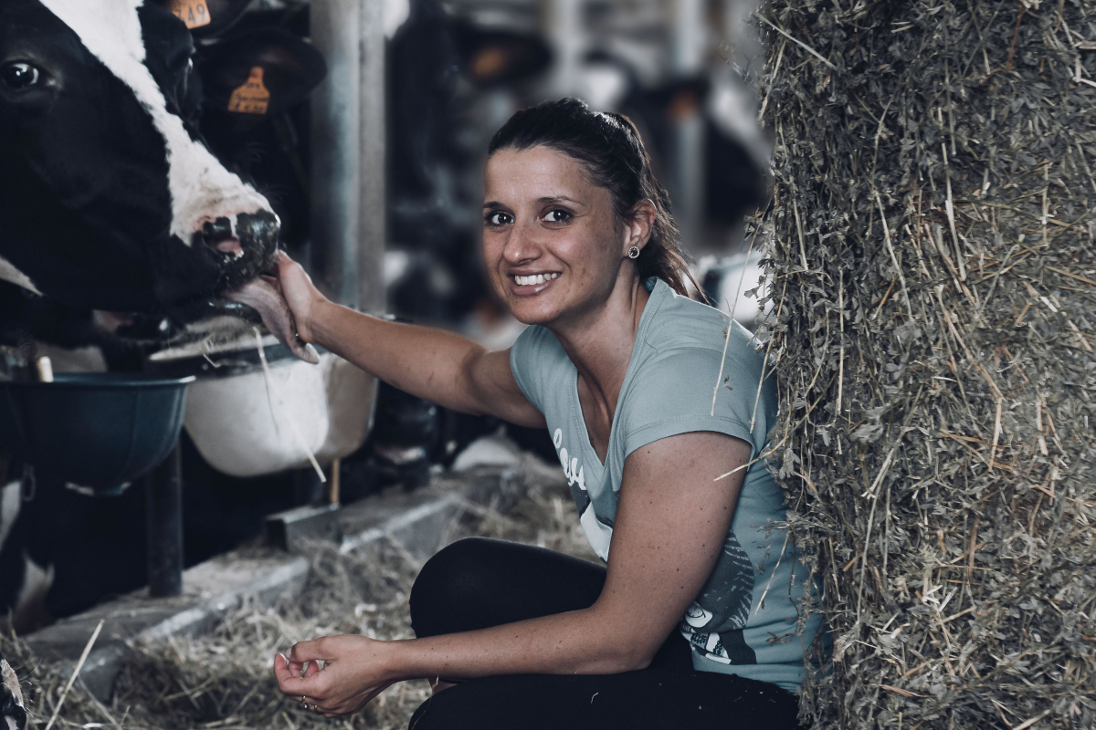 Donna sorridente accarezza mucca in stalla. Benessere animale, allevamento sostenibile, azienda agricola DalterFood.