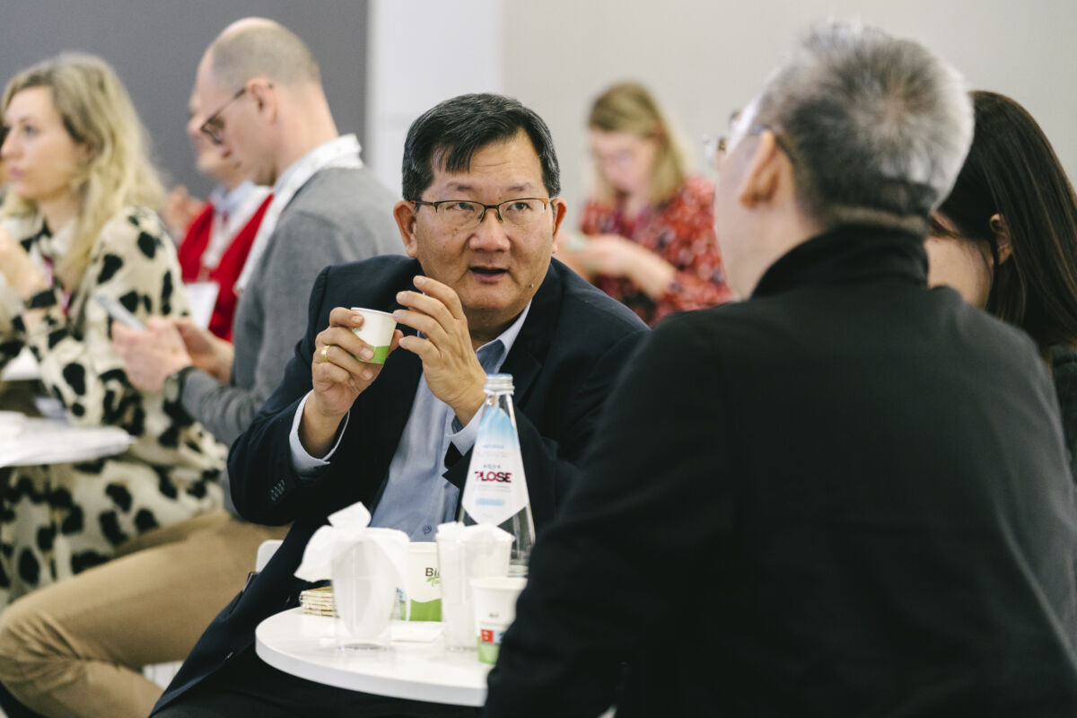 SANA Food 2025: Uomo asiatico con tazza a evento alimentare. Tavolo con acqua e bicchieri.