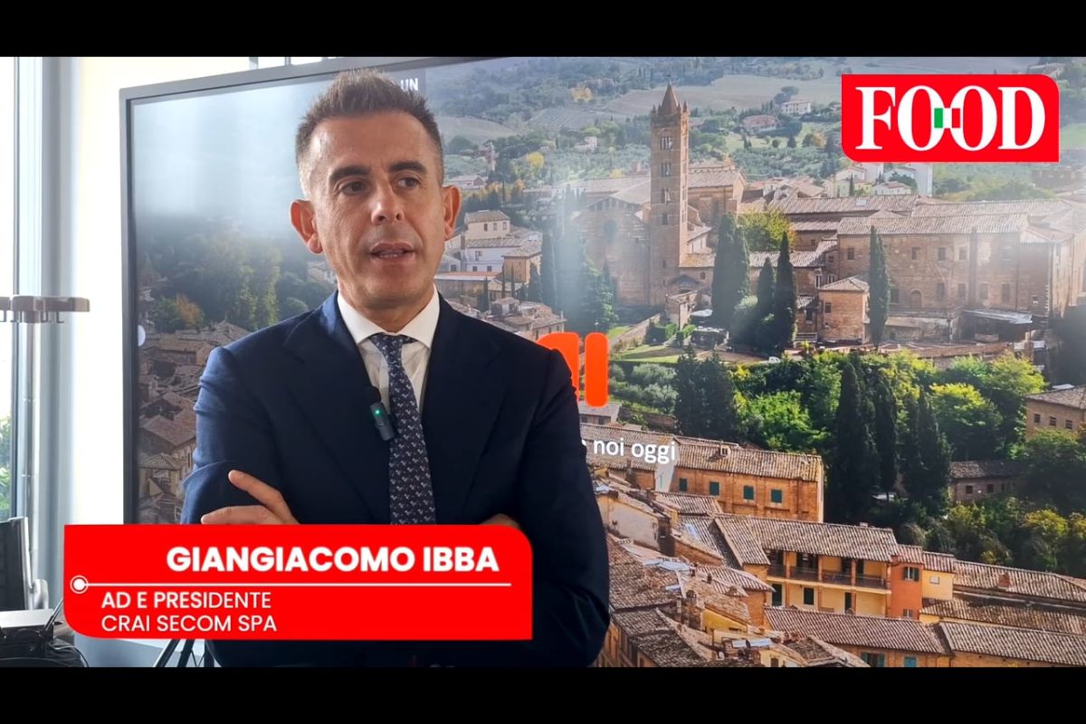 Giangiacomo Ibba, AD Crai Secom Spa, in primo piano. Borgo toscano e logo Food sullo sfondo.