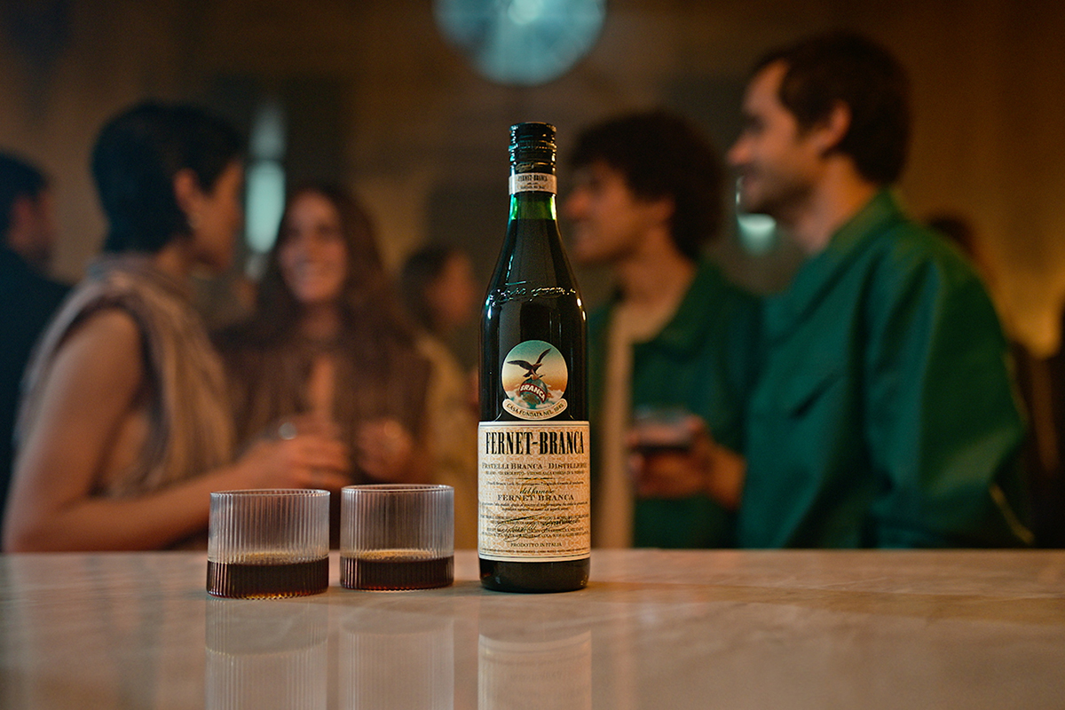 Bottiglia Fernet-Branca con bicchieri e persone. Amaro digestivo italiano dal 1845.