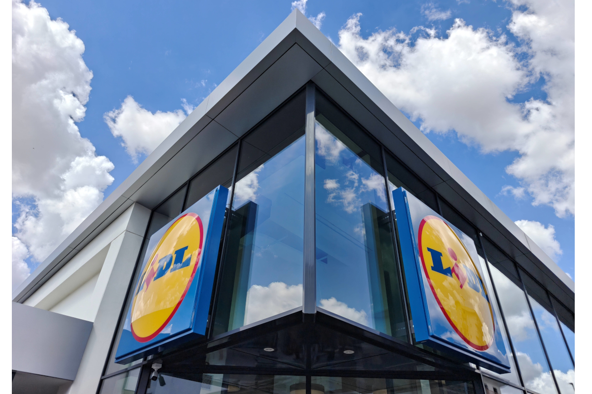 Ingresso Lidl con insegna blu e gialla. Facciata moderna, cielo azzurro con nuvole. Discount alimentare.
