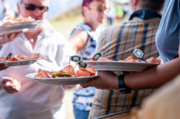 Degustazione Speck Alto Adige IGP. Piatti di speck con bandierine e cetriolini. Festa dello speck a Plan de Corones.