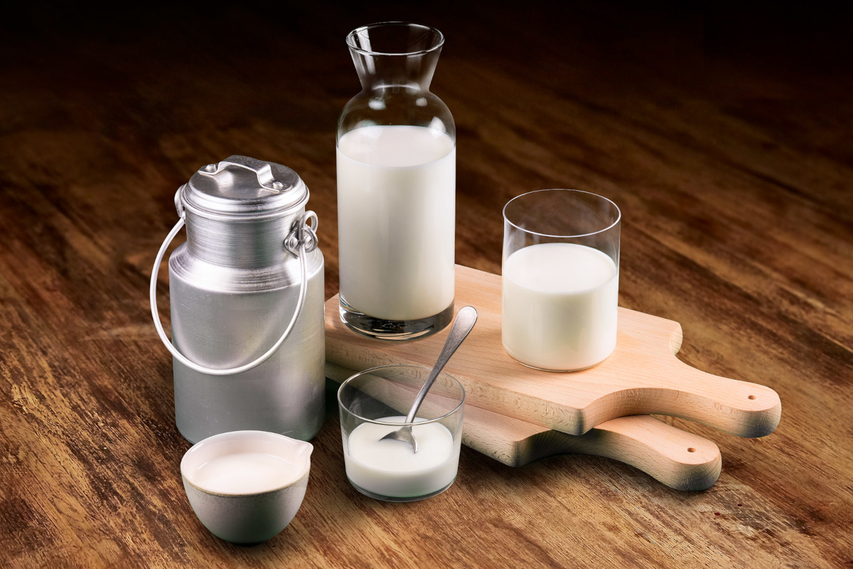 Latte fresco in brocca, bicchieri e lattiera su tagliere di legno. Foto di latte intero.