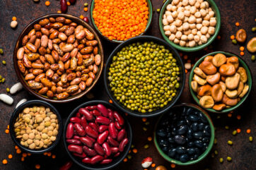 Varietà di legumi secchi in ciotole: lenticchie, fagioli, ceci, fave, piselli. Fonte di proteine vegetali.