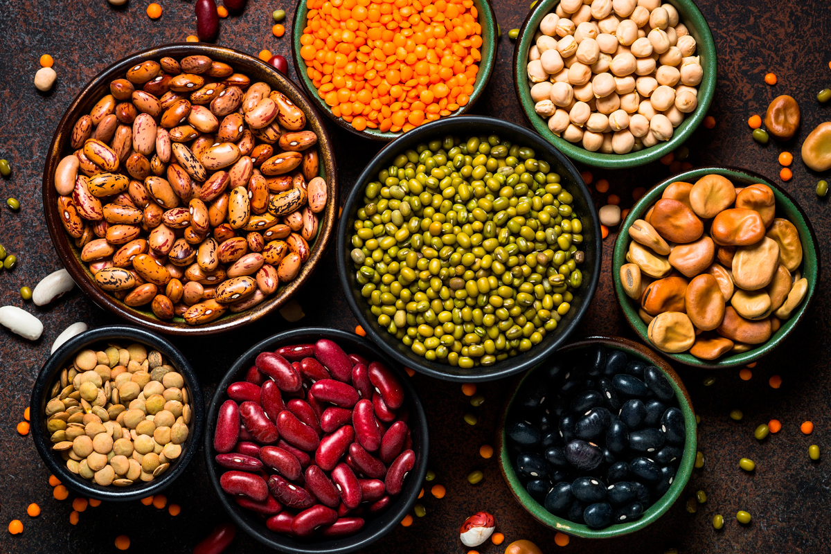 Varietà di legumi secchi in ciotole: lenticchie, fagioli, ceci, fave, piselli. Fonte di proteine vegetali.
