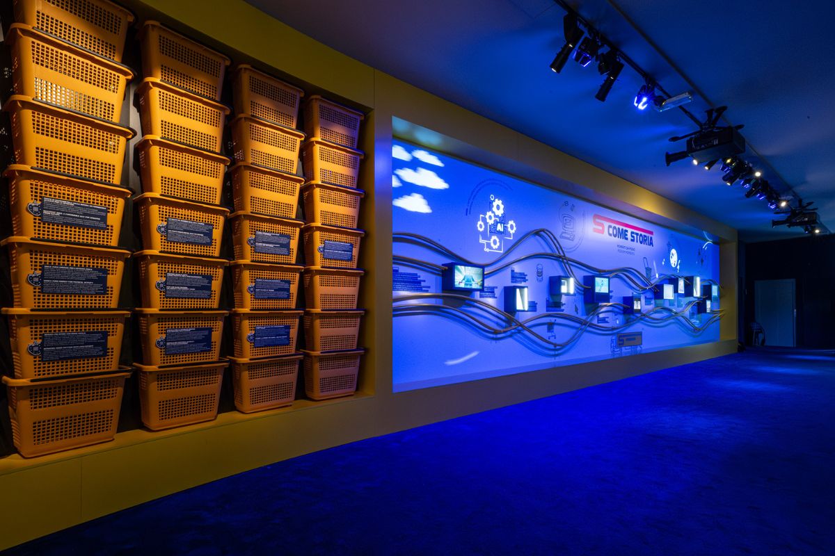 Casa Esselunga Milano Cortina 2026: esposizione con ceste gialle e pannello Come Storia illuminato di blu.