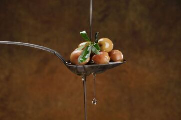 Olio extra vergine d'oliva su cucchiaio con olive. Rito quotidiano italiano.