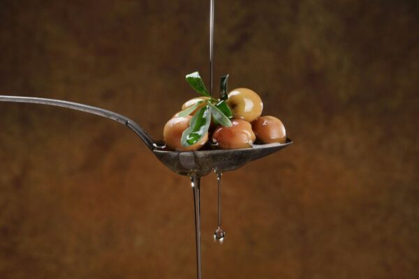 Olio extra vergine d'oliva su cucchiaio con olive. Rito quotidiano italiano.