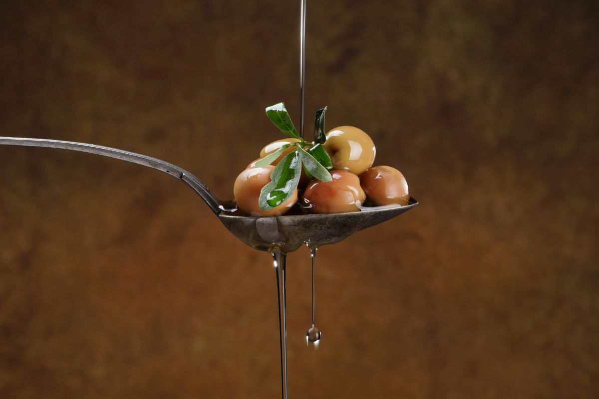 Olio extra vergine d'oliva su cucchiaio con olive. Rito quotidiano italiano.