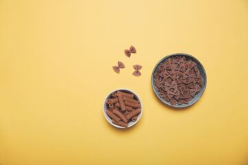 Pasta integrale: farfalle e rigatoni in ciotole su sfondo giallo. Alimenti salutistici e biologici.