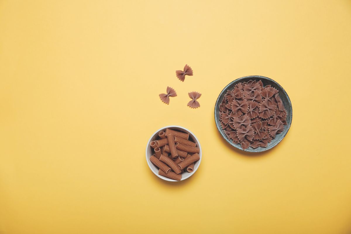Pasta integrale: farfalle e rigatoni in ciotole su sfondo giallo. Alimenti salutistici e biologici.