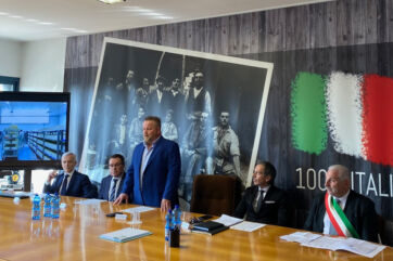 Conferenza stampa italiana: uomini in giacca e cravatta a un tavolo, bandiera italiana sullo sfondo. - Latterie Venete-Latterie VicentineCa.Form-Centro Veneto Formaggi