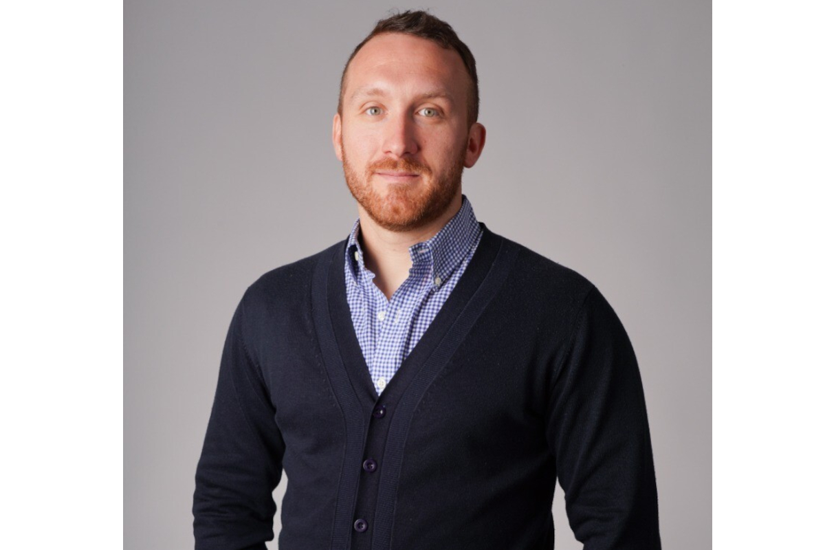 Rom'antica - Ritratto di Michele Mannara. Uomo caucasico con barba rossa, indossa camicia a quadri e cardigan blu. Sfondo grigio.