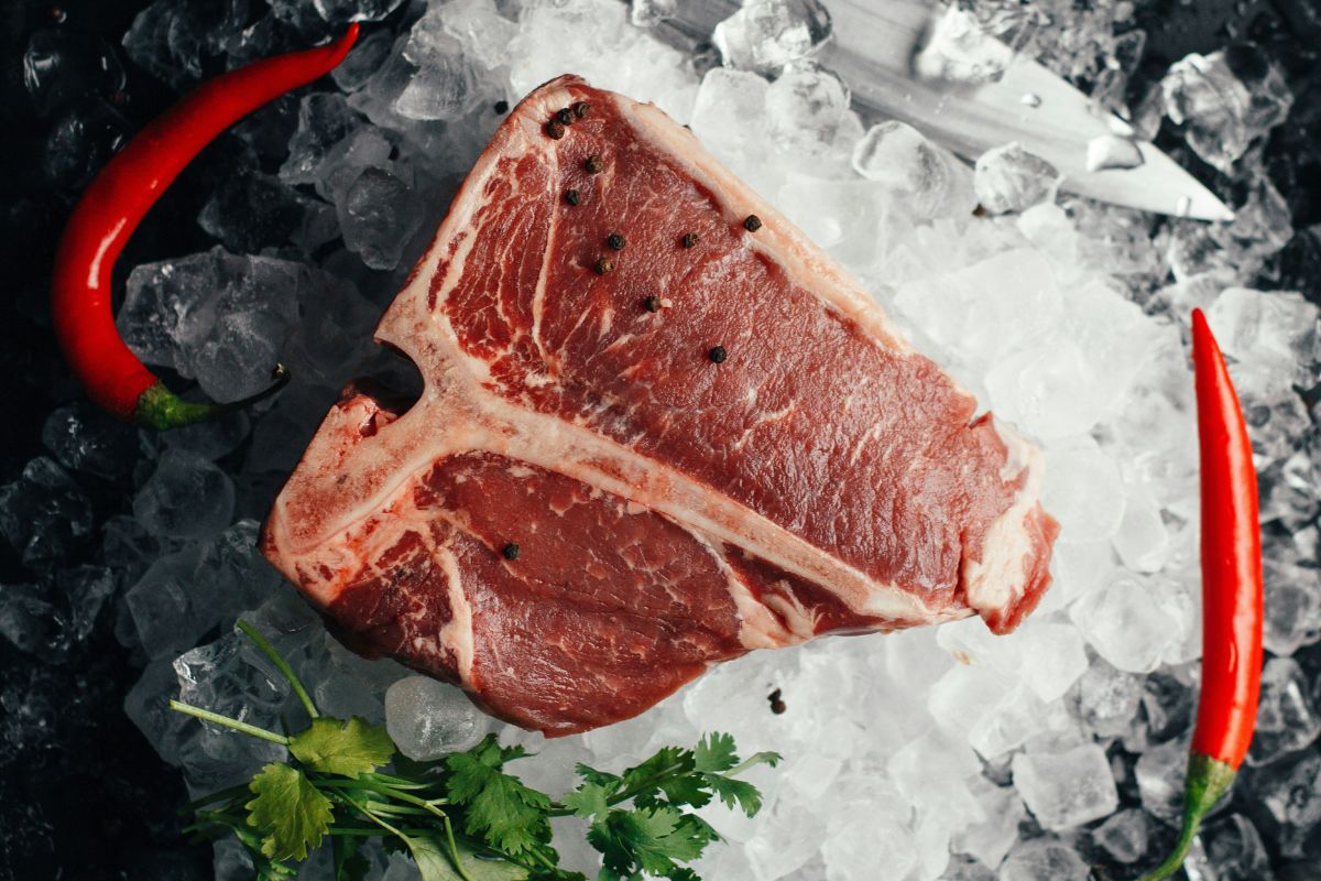 Bistecca di carne surgelata su ghiaccio con peperoncino. Taglio pregiato, ideale per grigliate e ricette gourmet.