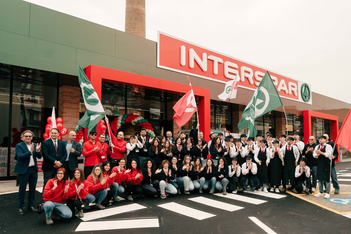 Maiora-Inaugurazione Interspar: gruppo di persone festeggiano davanti al nuovo supermercato. Bandiere e sorrisi.