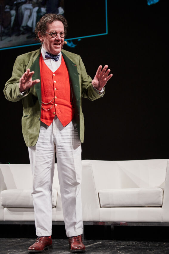 Relatore al Food Summit 2018. Uomo con papillon, gilet rosso e giacca verde parla sul palco. Community e incontri.