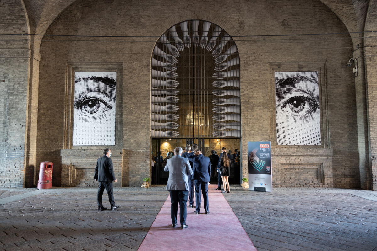 Ingresso al FOOD Summit 2021. Persone in fila, occhi giganti e tappeto rosso.