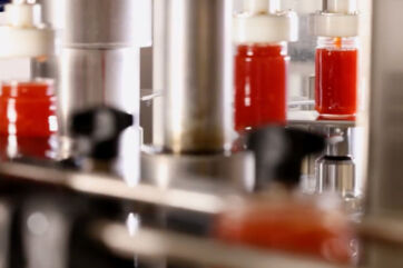 Produzione Agrisicilia: vasetti di marmellata rossa su linea di confezionamento industriale. Alimenti siciliani.