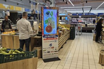 AI nel reparto ortofrutta: display digitale ALDO con frutta e verdura al supermercato. Assistente AI per la spesa.