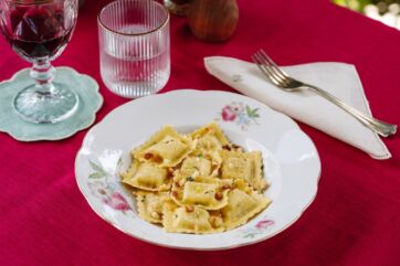 Ravioli artigianali del Ravioificio Scoiattolo. Piatto di pasta fresca ripiena, vino rosso e acqua.