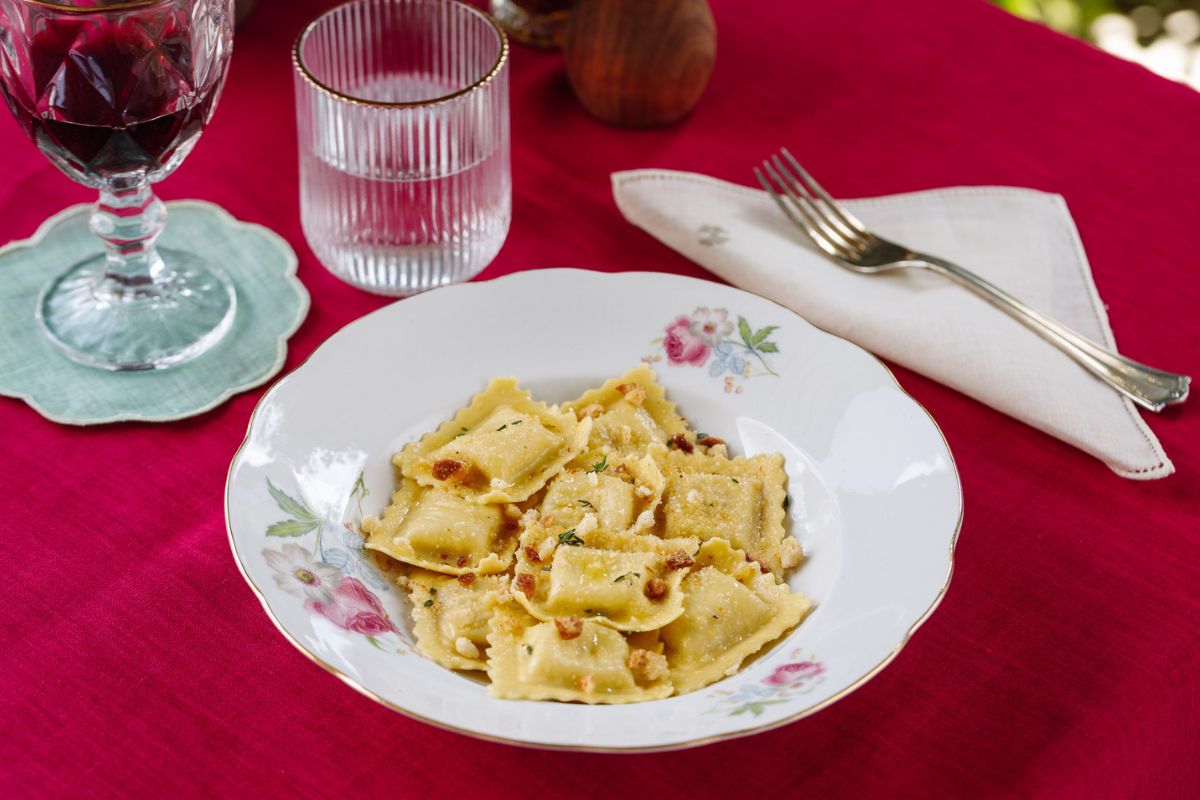 Ravioli artigianali del Ravioificio Scoiattolo. Piatto di pasta fresca ripiena, vino rosso e acqua.