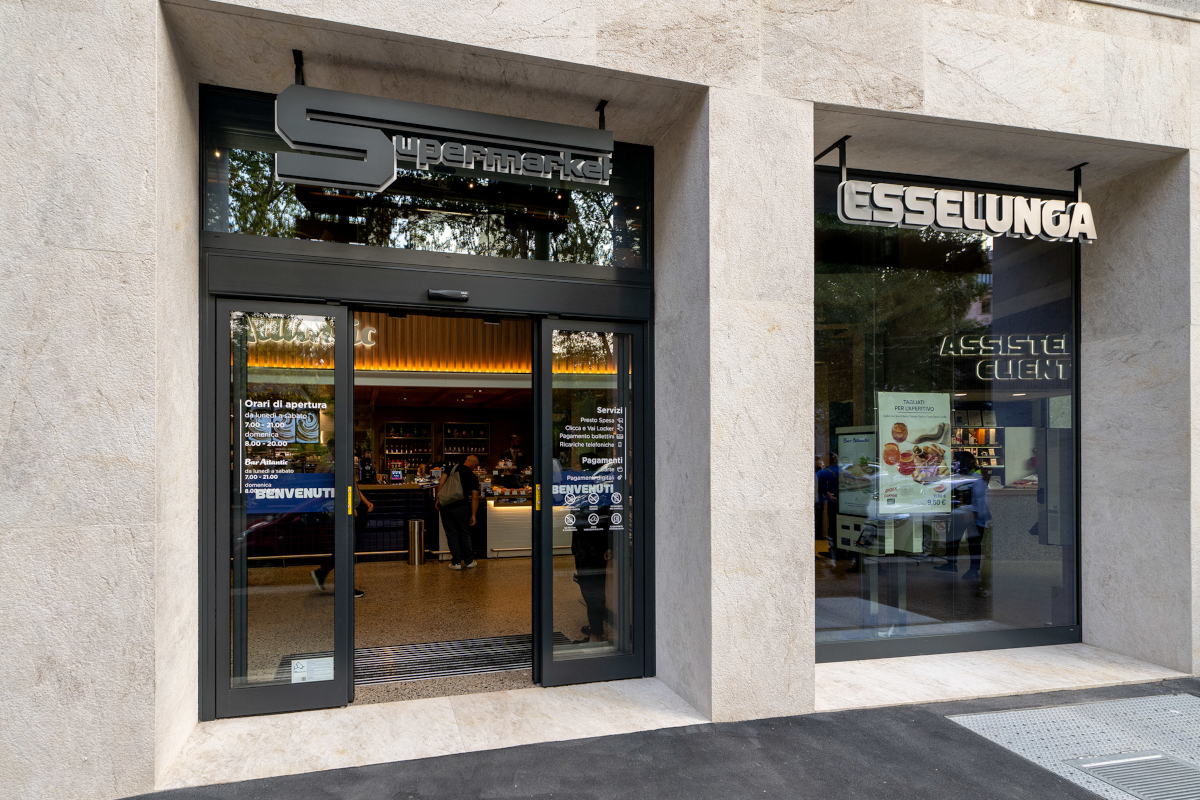 Ingresso di un punto vendita Esselunga con insegna Supermarket, porte automatiche e vetrine in un moderno edificio.