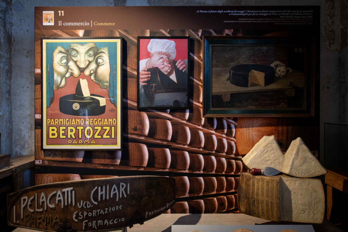 Esposizione storica del Museo del Parmigiano Reggiano con manifesti pubblicitari, forme di formaggio e pannelli informativi.