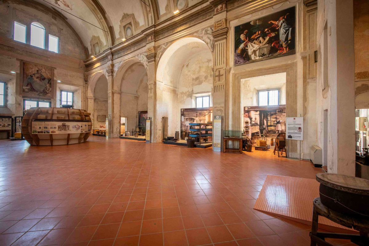 Interno del Museo del Parmigiano Reggiano con ampie sale, archi storici, esposizioni tematiche e pavimentazione in cotto.