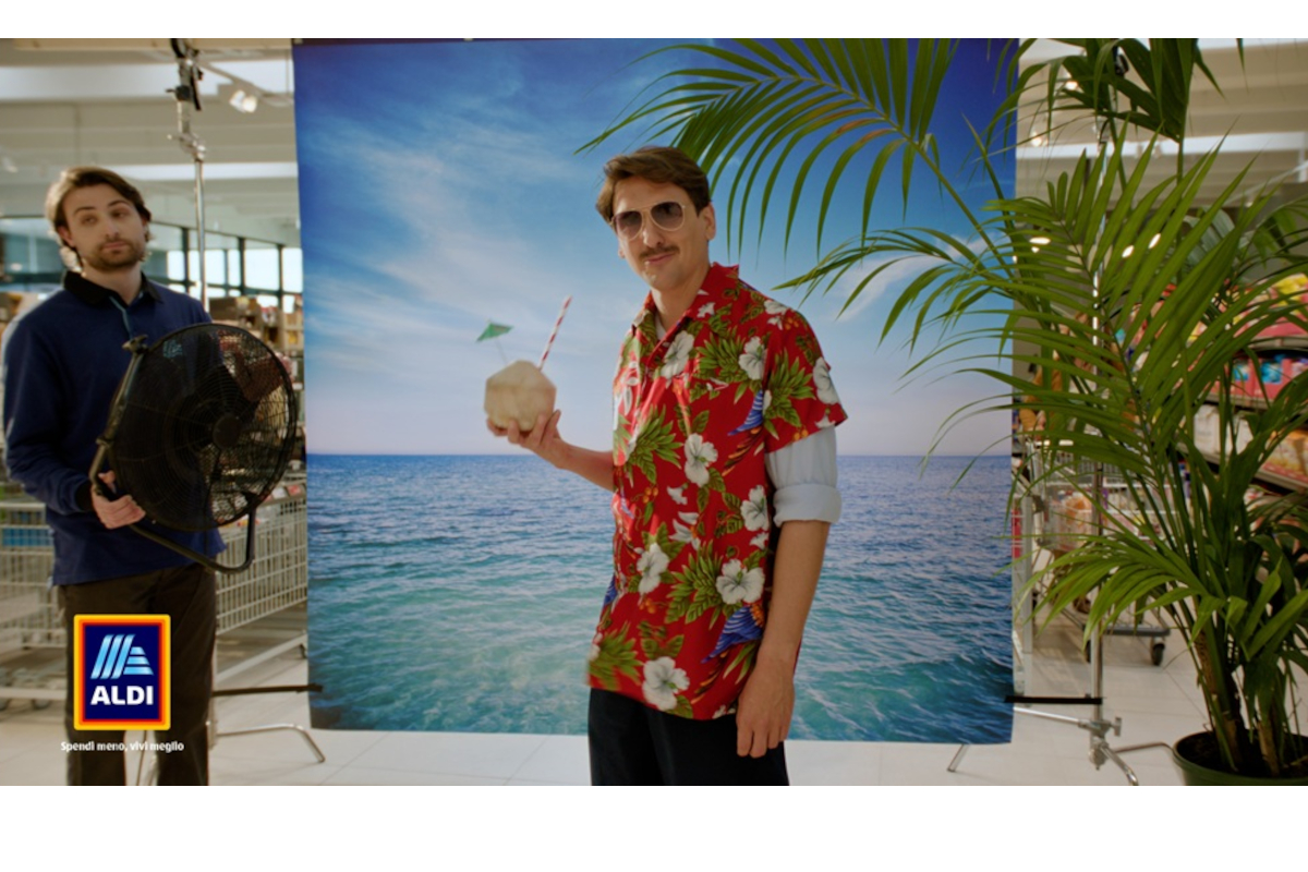Aldi-Uomo con camicia hawaiana e cocco davanti a uno sfondo marino per la campagna pubblicitaria The Cheapest Campaign Aldi.
