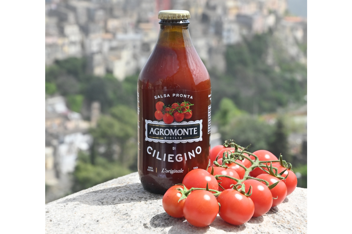 Bottiglia di Salsa Pronta di Ciliegino Agromonte con pomodorini freschi su sfondo paesaggistico siciliano.