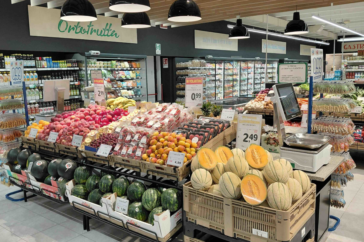 Reparto ortofrutta del supermercato Ama Crai Est a Villa Estense con esposizione di frutta fresca e meloni in vendita.