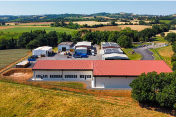 Veduta aerea della sede di Apicoltura Piana con capannoni industriali, pannelli solari e campi coltivati circostanti.