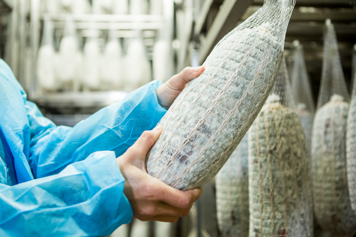 Addetto controlla la stagionatura di una Bresaola della Valtellina Igp in una cella di produzione industriale.