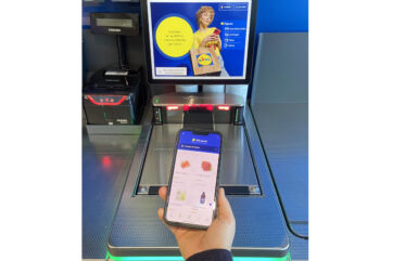 Cliente usa l'app Lidl Plus su smartphone per pagare alla cassa automatica Toshiba in un supermercato Lidl.