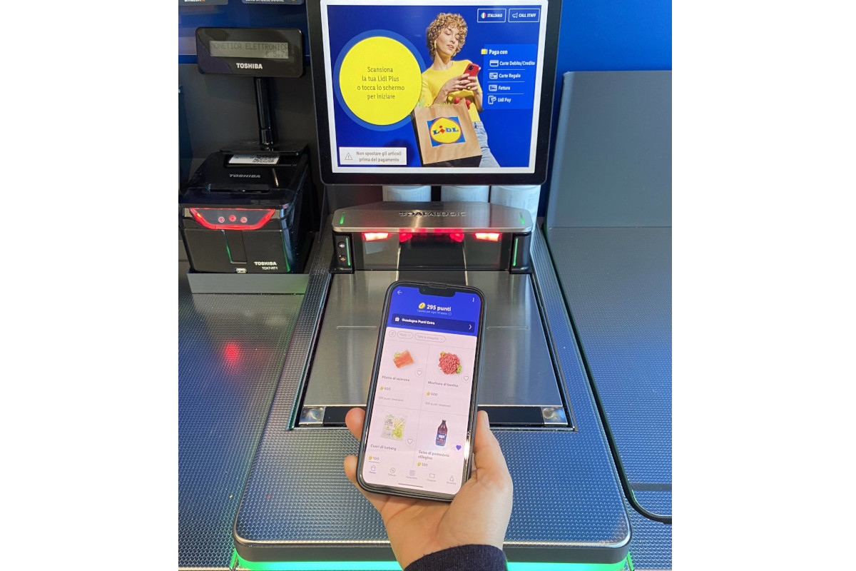 Cliente usa l'app Lidl Plus su smartphone per pagare alla cassa automatica Toshiba in un supermercato Lidl.