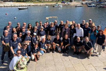 Gruppo di persone con magliette blu alla Convention Coralis 2026 posa per una foto ricordo presso il porto turistico.